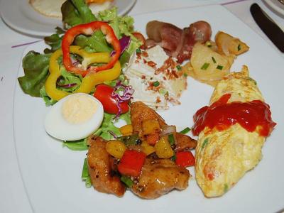 Vielseitiges Frühstück mit Omelett, gekochtem Ei, gebratenem Gemüse, Speck und Salat auf weißem Teller.