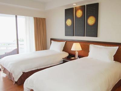 Hell eingerichtetes Zimmer mit zwei Einzelbetten, Nachttisch, Lampe und dreiteiligem Wandbild.