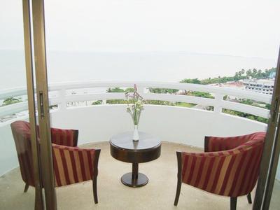 Balkon mit zwei rot gestreiften Sesseln und kleinem runden Tisch, dahinter Meerblick bei trübem Himmel.