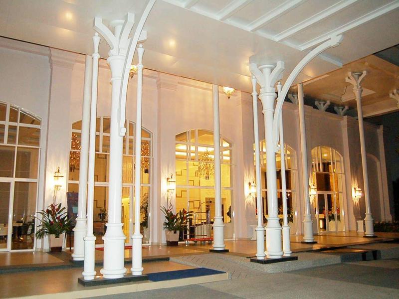 Eingang mit weißen Säulen, großen Fenstern und warmem Licht im Innenraum bei Nacht.