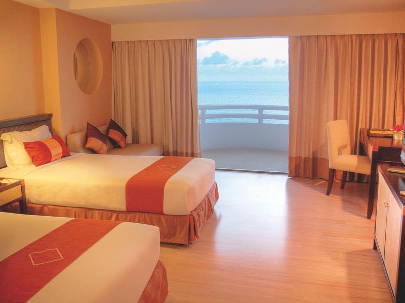 Helles Hotelzimmer mit zwei Betten, orangefarbenen Akzenten und Balkon mit Meerblick.