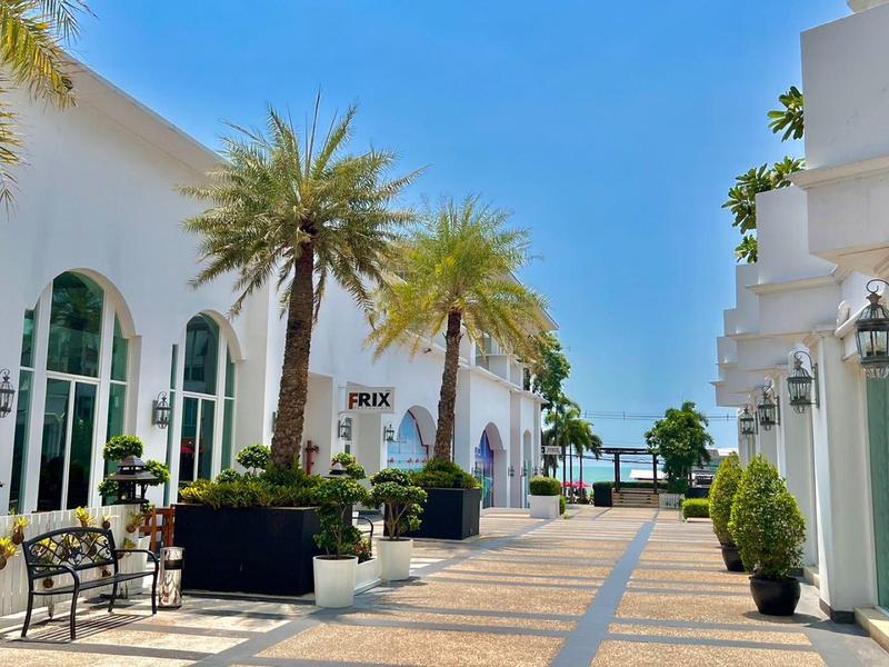 Breite Promenade mit weißen Gebäuden, Palmen und Bänken unter klarem blauem Himmel.