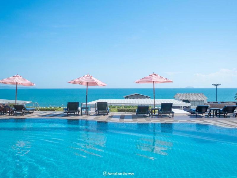 Pool mit klar blauem Wasser, pinken Sonnenschirmen und Blick auf das blaue Meer unter klarem Himmel.