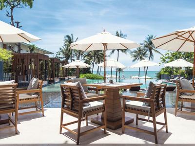 Außenbereich eines Resorts mit Holzmöbeln und weißen Sonnenschirmen am Pool