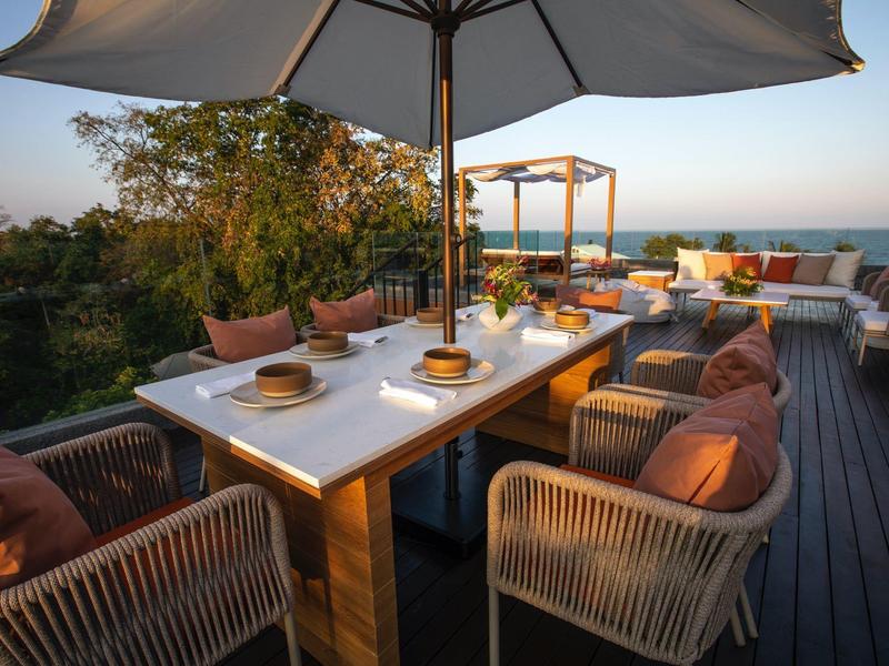 Moderne buitenterras met grote eettafel, comfortabele stoelen en zonnescherm bij zonsondergang.