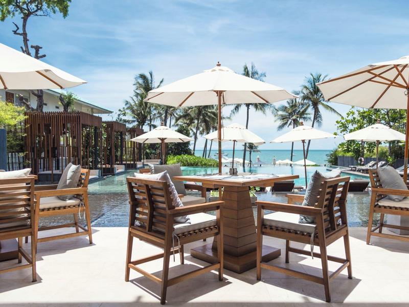 Buitenloungegebied met stoelen, tafels en parasols bij een hotelresort.