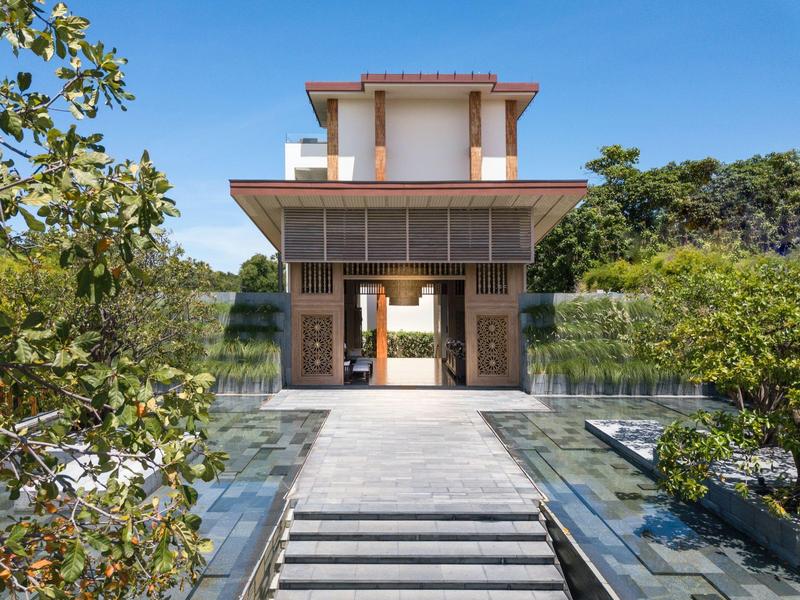 Moderne gebouwentree met brede weg en waterpartijen aan beide zijden, omgeven door bomen.