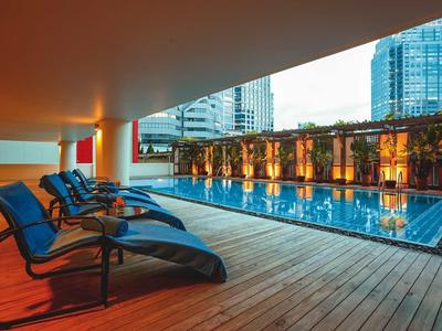 Moderner Pool auf Dachterrasse mit Liegestühlen und Stadtgebäuden im Hintergrund bei Sonnenuntergang.