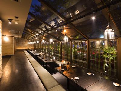 Langes, modernes Restaurant mit Glasdach, beleuchteten Tischen und gemütlichen Sitzbänken bei Nacht.