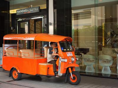 Oranger Tuk-Tuk mit offenem Fahrerbereich steht vor Glasfassade eines Gebäudes.