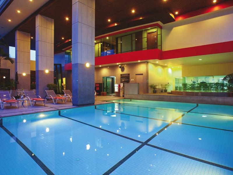 Moderner Außenpool bei Nacht mit beleuchtetem Wasser, gepolsterten Liegestühlen und Glasfenstern.