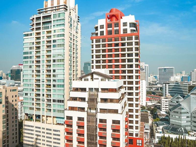 Mehrstöckige Gebäude mit Glasfenstern und roten Balkonen unter klarem blauen Himmel.