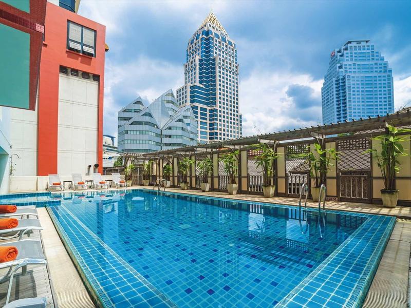 Ein klarer blauer Pool mit Liegestühlen auf der linken Seite und hohen Gebäuden im Hintergrund.