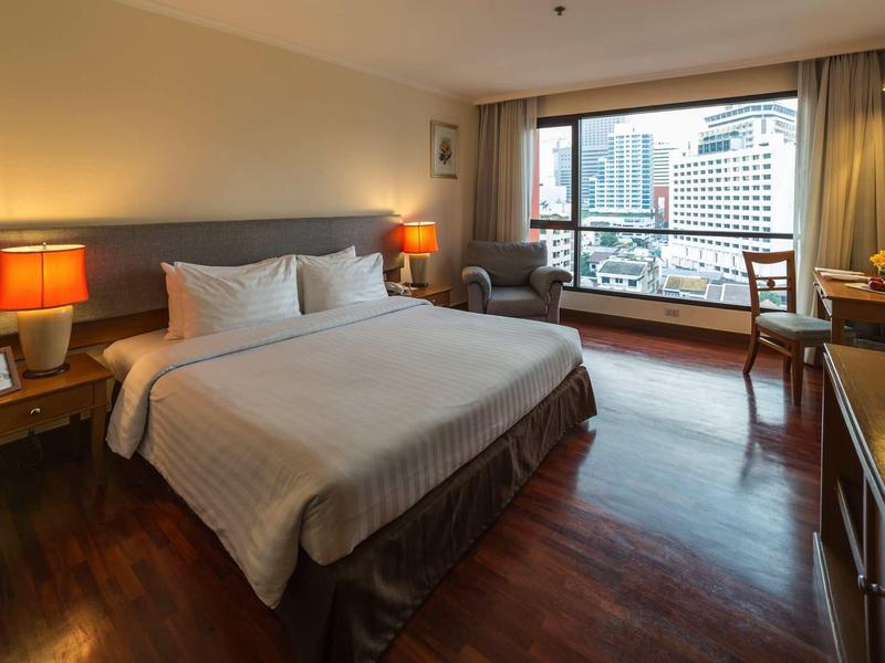 Modernes Hotelzimmer mit großem Bett, Holzboden, Fensterblick auf Stadt und warmem Licht.