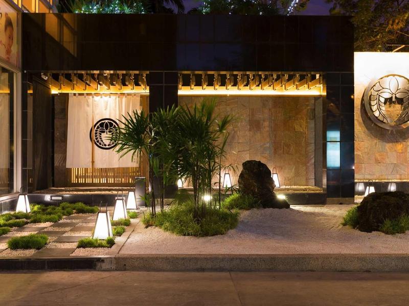 Moderner Innenhof bei Nacht mit Pflanzen, Steinen und warmem Licht auf dem Boden.