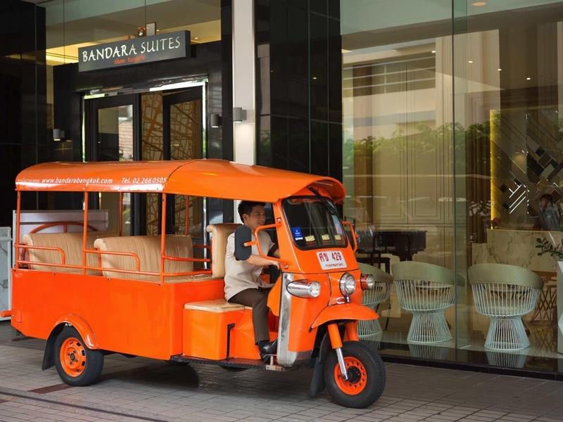 Oranger Tuk-Tuk mit offenem Fahrerbereich steht vor Glasfassade eines Gebäudes.