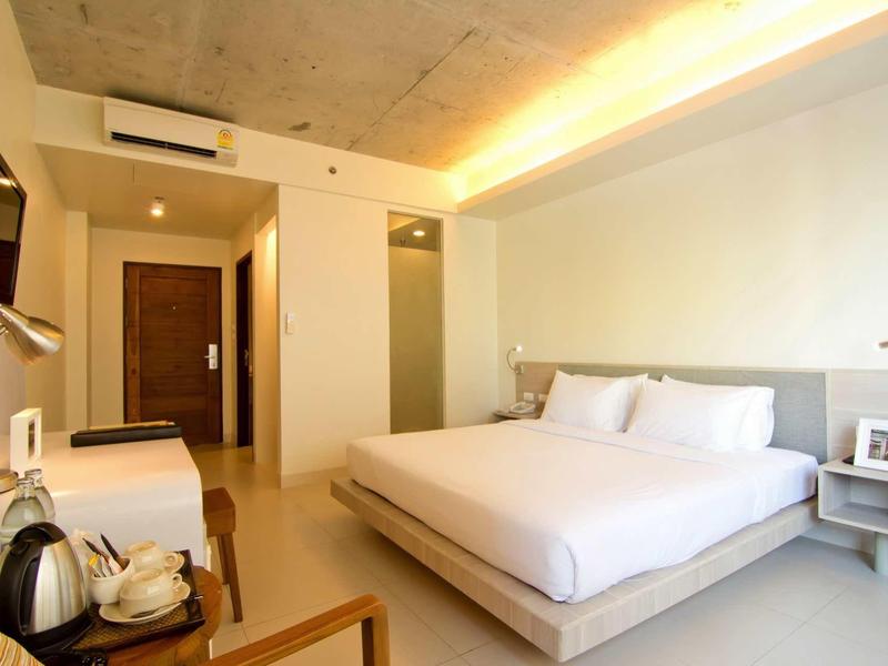 Helles, modernes Schlafzimmer mit großem Bett, Holzstuhl, Fernseher und Klimaanlage an der Decke.