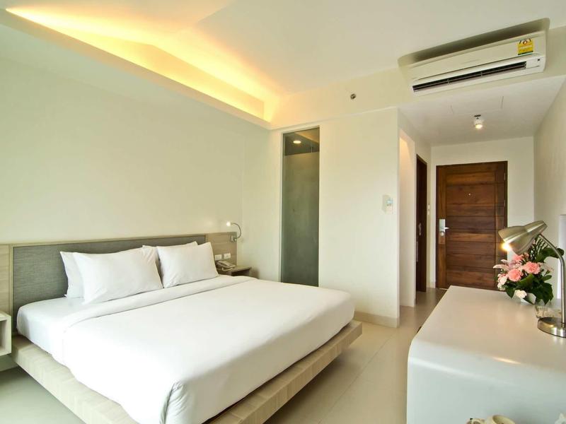 Helles Schlafzimmer mit großem Bett, weißer Bettwäsche, Klimaanlage und Fernseher an der Wand.