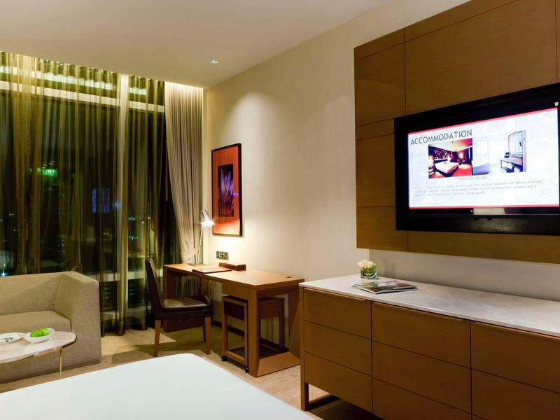 Modernes Hotelzimmer mit großem Fenster, Schreibtisch, Sofa und Wand-TV in warmem Licht.