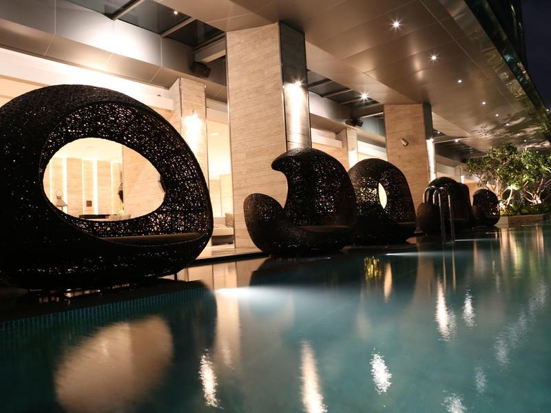 Moderne, geschwungene Sitzmöbel neben beleuchtetem Pool in eleganter, nächtlicher Architektur.