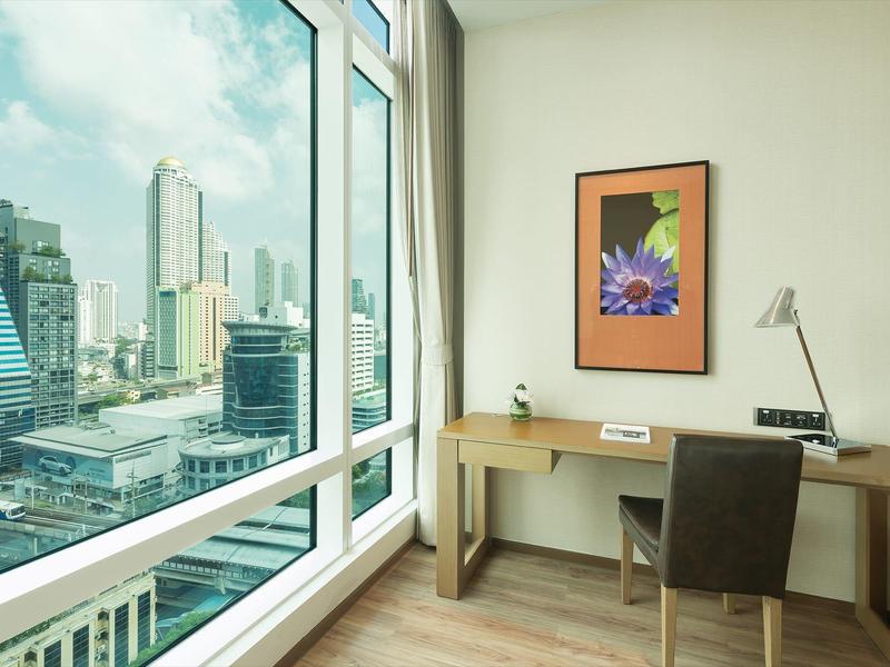 Moderner Arbeitsplatz mit großem Fenster, hölzernem Schreibtisch, Stuhl und gerahmtem Blumenbild.