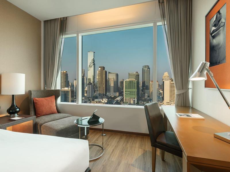 Modern eingerichtetes Wohnzimmer mit grasem Sofa, Holzboden, Schreibtisch und großer Fensterfront zur Stadt.