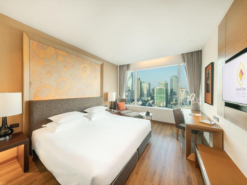 Modernes Hotelzimmer mit großem Bett, Holzfußboden, Schreibtisch und Blick auf Stadtskyline.