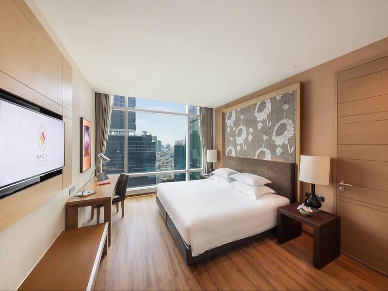 Modernes Hotelzimmer mit großem Bett, Schreibtisch, Fernseher und Panoramafenster mit Stadtblick.