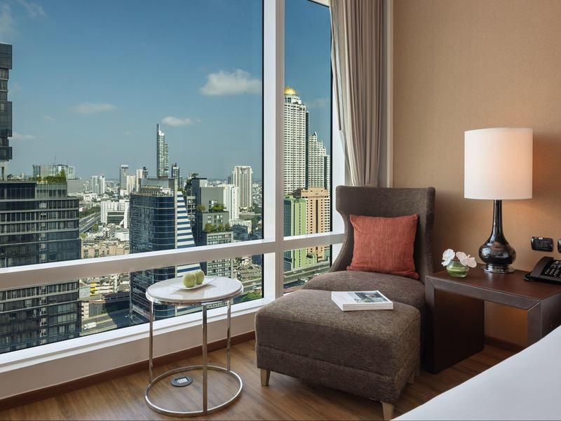 Moderner Sitzbereich mit braunem Sessel, Beistelltisch und großer Fensterfront mit Stadtblick.