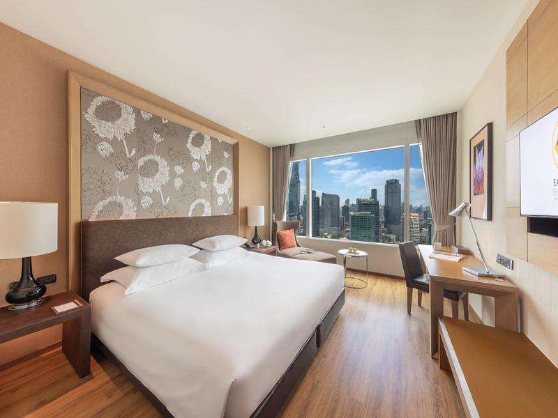 Modernes Schlafzimmer mit großem Bett, Holzboden, Schreibtisch und Panoramafenster mit Stadtblick.