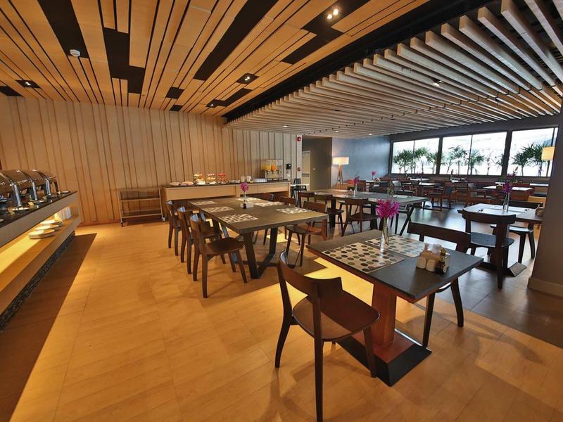 Moderner Gastraum mit Holztischen, Stühlen und Holzdeckenleisten, hell beleuchtet durch Fenster.