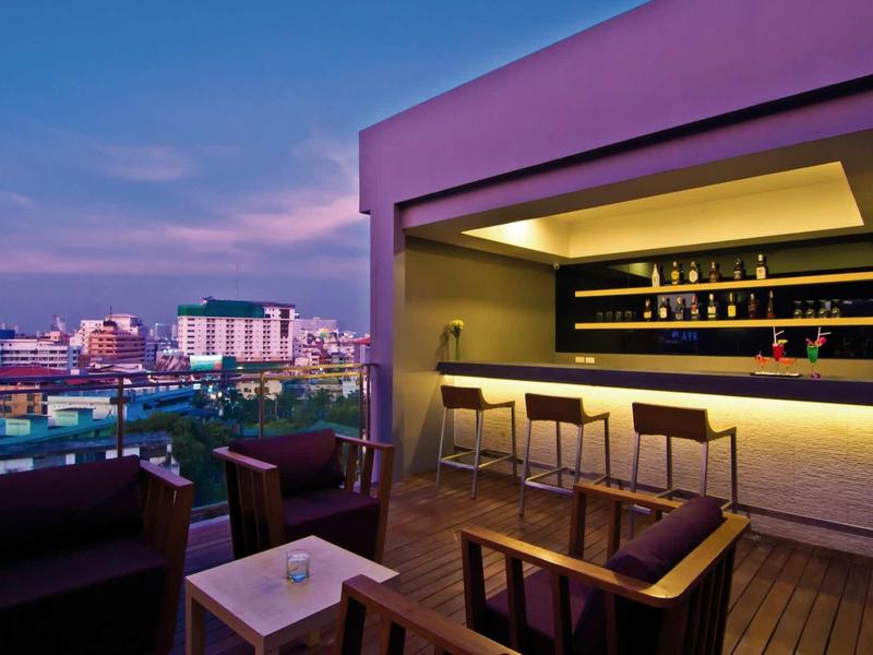 Moderne Dachterrasse mit Bar, Hockern und Sitzgruppe, im Hintergrund Stadt bei Sonnenuntergang.