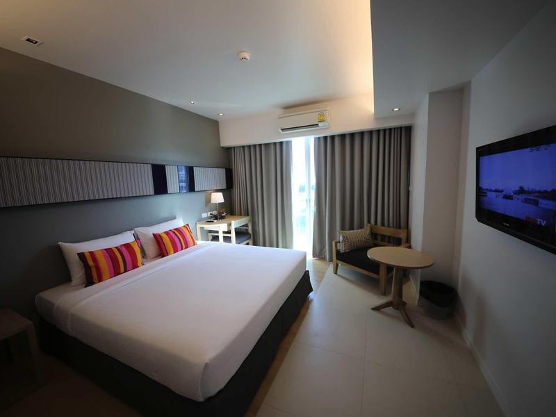 Modernes Hotelzimmer mit großem Bett, schlichter Einrichtung, TV an der Wand und Fenster mit Vorhängen.