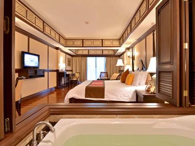 Luxurious hotel room with double bed, large mirror, and bathtub overlooking the space.