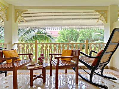 Cozy porch with wooden chairs, table, and greenery view in daylight.