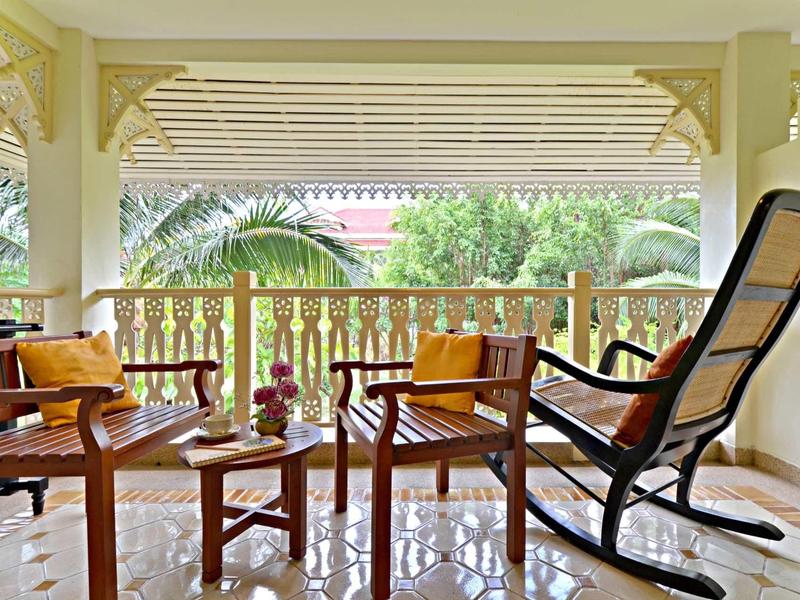 Cozy porch with wooden chairs, table, and greenery view in daylight.