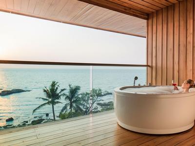 Runde Badewanne auf Balkon mit Meerblick und Sonnenuntergang im Hintergrund.