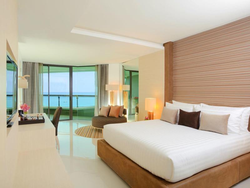 Modernes Hotelzimmer mit großem Bett, Holzdekor, Sitzbereich und Blick auf das Meer durch große Fenster.