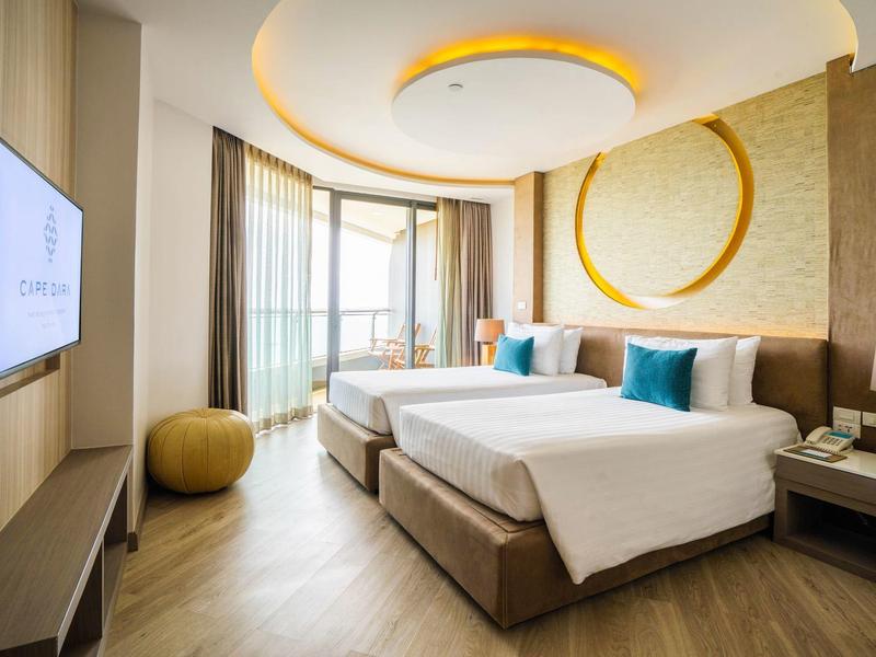 Modernes Hotelzimmer mit zwei Betten, großen Fenstern, Holzfußboden und warmen Gelbtönen.