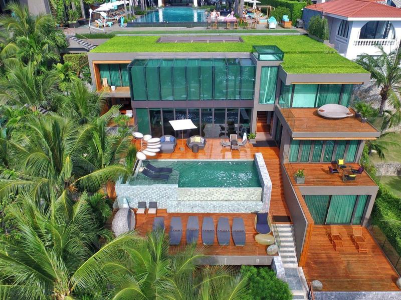 Moderne Villa mit Glasfront, Terrasse, Pool, umgeben von Palmen und grünen Flächen an Hanglage.