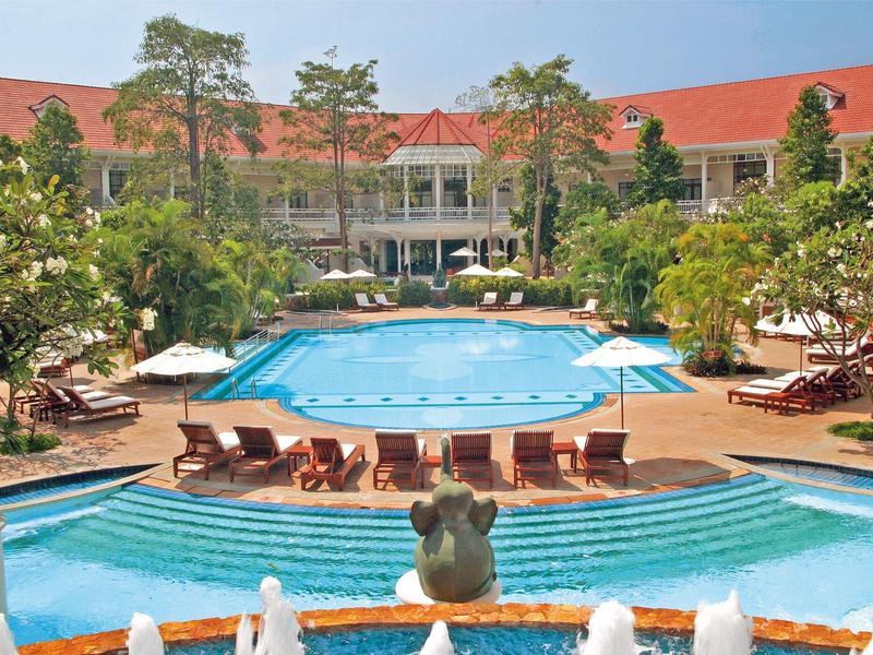 Groot hotelzwembad met ligstoelen, parasols en weelderig groen eromheen.