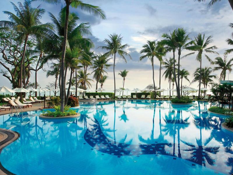 Helderblauw zwembad omringd door palmbomen en ligstoelen bij zonsondergang.