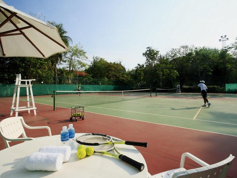 Buiten tennisbaan met een speler en een overdekte zitplek met handdoeken, water en rackets.