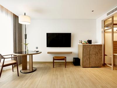 Helles, modernes Wohnzimmer mit Holzfußboden, TV an der Wand, runden Tisch und Stühlen neben Fenster.