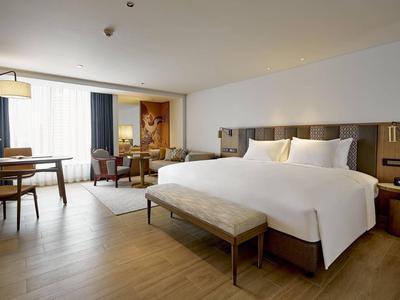 Helles Hotelzimmer mit großem Bett, Holzboden, Sitzbereich und Schreibtisch nahe Fenster.