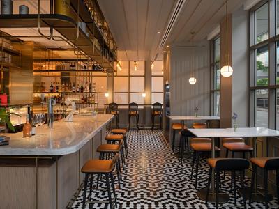 Modernes Restaurant mit Bar, hohen Hockern und schwarz-weißem geometrischem Fliesenboden.