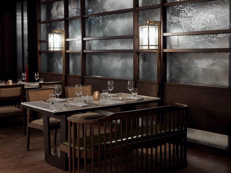 Gemütlicher Restaurantbereich mit dunklem Holz, Lampen und gedecktem Tisch mit Gläsern und Besteck.