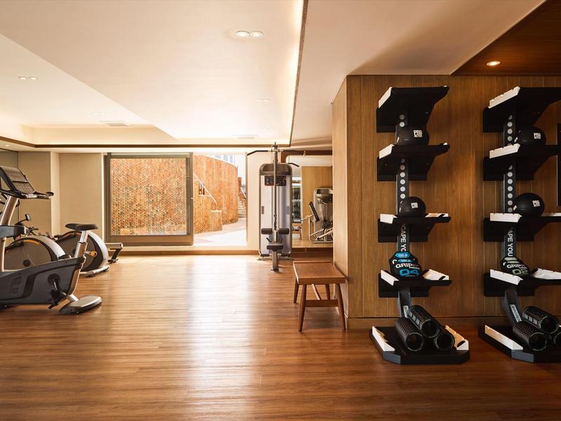 Moderner Fitnessraum mit Holzboden, Trainingsgeräten und Hanteln an der Wand.