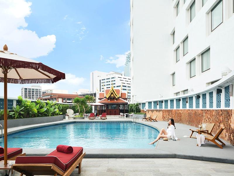 Moderner Außenpool mit Liegestühlen, Sonnenschirm und städtischer Kulisse im Hintergrund.