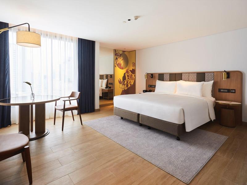 Modernes Hotelzimmer mit großem Bett, Holzmöbeln, Teppich und Fenster mit Vorhängen.